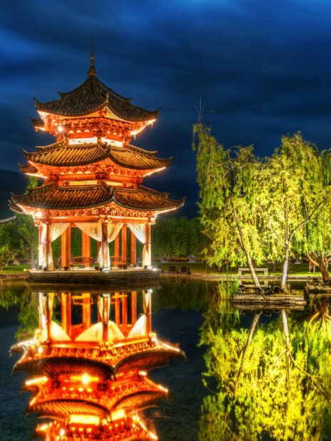Traditional Chinese pavilion illuminated at night reflecting in calm water