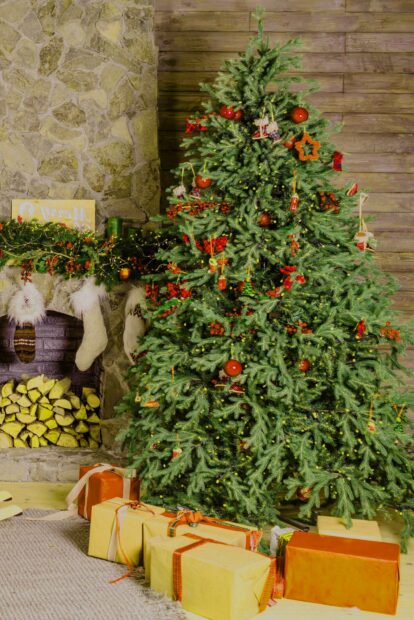 A decorated Christmas tree with red ornaments and presents near a stone fireplace