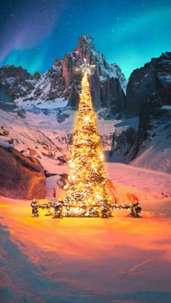 A glowing Christmas tree surrounded by snow in a mountainous winter landscape