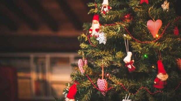 A Christmas tree decorated with heart shaped ornaments and small dolls on a wooden background