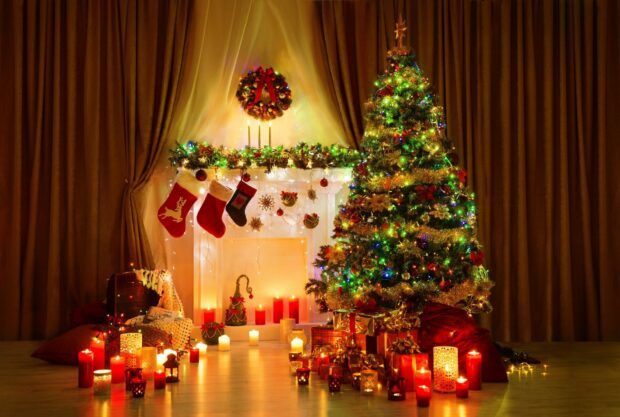 A beautifully decorated Christmas tree with colorful lights and presents near a fireplace with stockings and candles