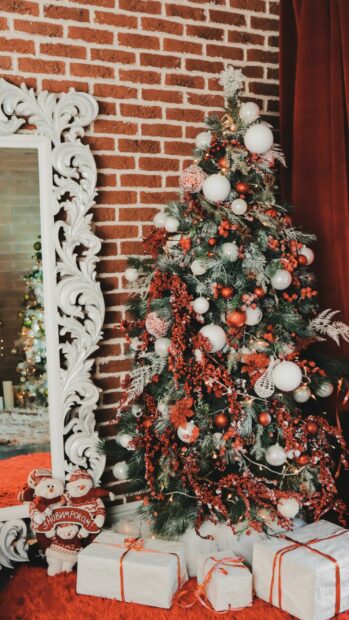 Christmas tree decorated with red berries and white ornaments in a cozy room with a brick wall and gifts
