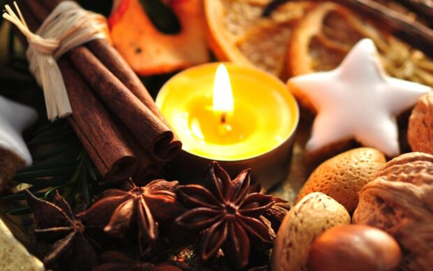 A close up of cinnamon sticks with star anise nuts and a lit candle surrounded by nuts and festive decorations