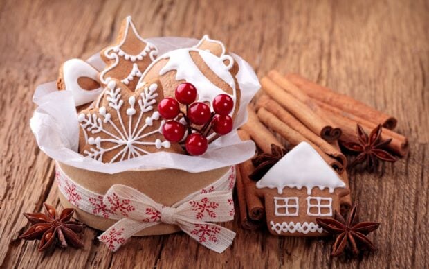 A festive arrangement of cinnamon sticks and decorated gingerbread cookies with red berries on a wooden surface