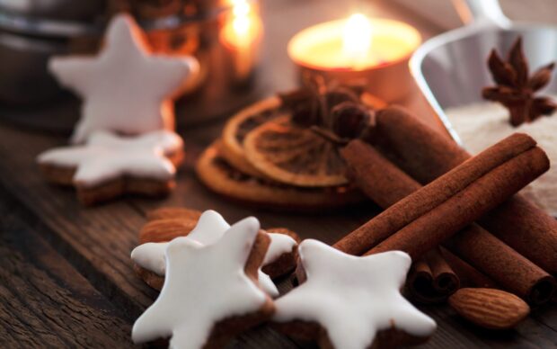 Star shaped cinnamon cookies with cinnamon sticks and a lit candle on wooden surface