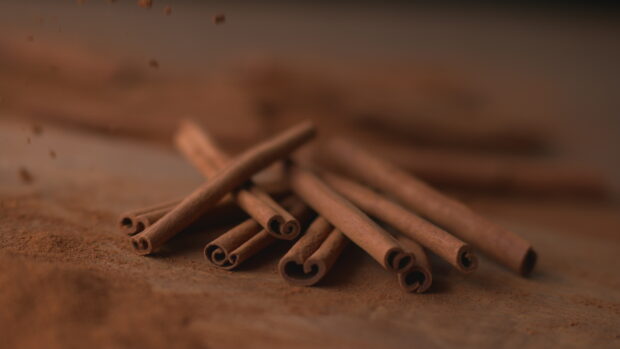 Close up view of cinnamon sticks neatly arranged on a wooden surface with cinnamon powder around