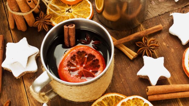 A cup of mulled wine with cinnamon sticks and dried orange slices on wooden table