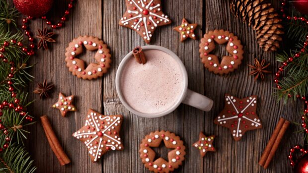 Cinnamon spice sticks and decorated cookies surround a cup of frothy cinnamon drink on a wooden table