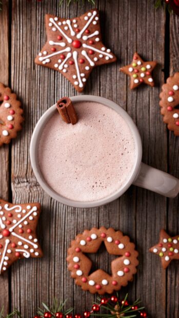 A frothy drink topped with a cinnamon stick surrounded by decorated gingerbread cookies on wood