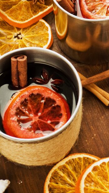 A warm drink with cinnamon sticks and orange slices on a wooden surface