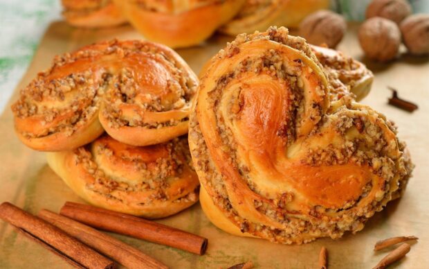 Close up of cinnamon swirled baked pastry with nuts and cinnamon sticks on table