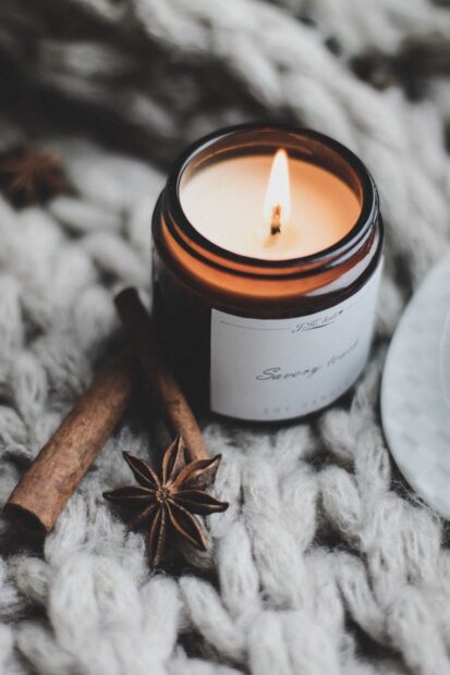 A burning candle with cinnamon sticks and star anise on a cozy knitted surface