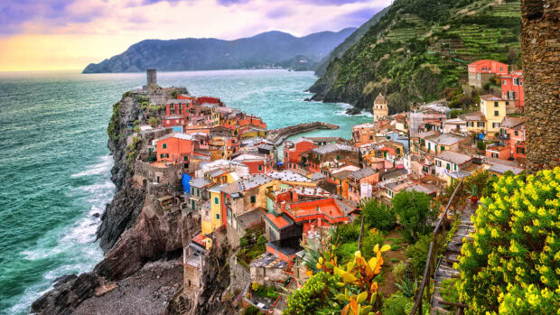 Colorful Cinque Terre village perched on rocky coastline with lush greenery and turquoise sea