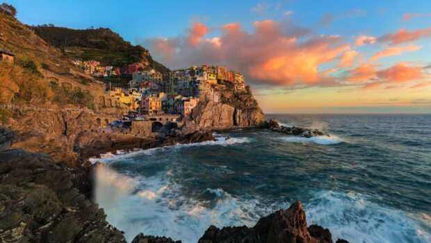 Colorful Cinque Terre village on rocky coastline during sunset with waves crashing