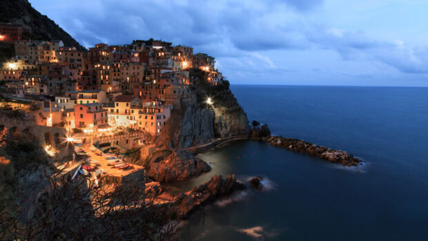 The Cinque Terre coastal village glowing with lights at dusk against the sea and sky
