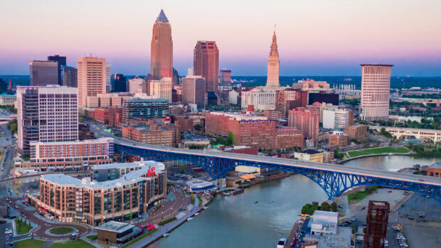 A view of Cleveland city skyline with urban buildings and a blue bridge over the river at sunset