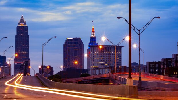 The Cleveland city skyline with illuminated buildings and light trails on the highway at dusk