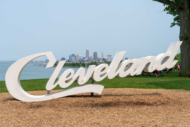 The Cleveland city skyline with a large Cleveland sign in the foreground on a sunny day