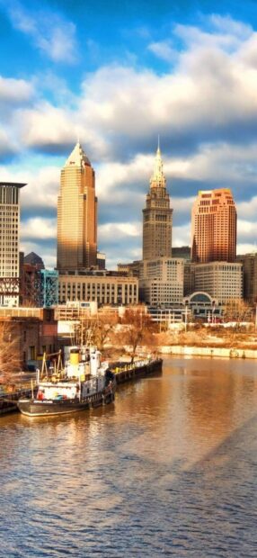 A scenic view of Cleveland skyline with river and boats in golden sunlight