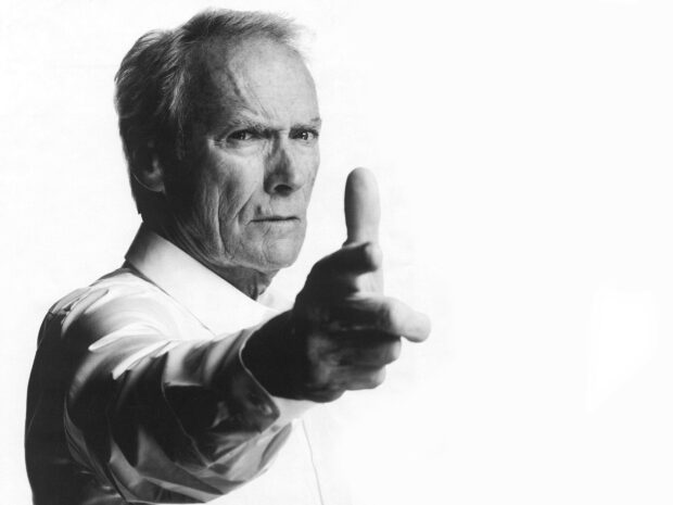 Clint Eastwood posing with his hand shaped like a gun in a black and white portrait