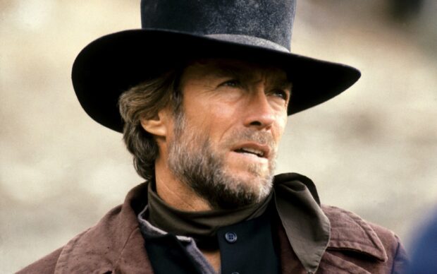 Clint Eastwood wearing a cowboy hat and scarf looking serious in a western setting