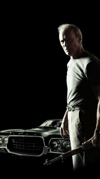 Clint Eastwood holding a rifle standing next to a classic car in a dark setting