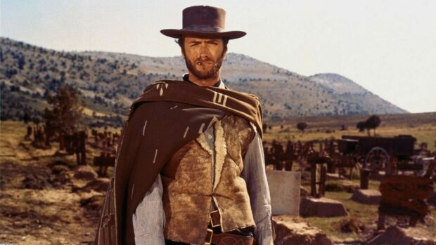 Clint Eastwood wearing a brown hat and poncho standing in a western graveyard scene