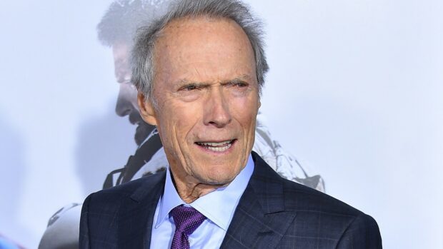 Clint Eastwood wearing a dark suit and purple tie with a serious expression at an event