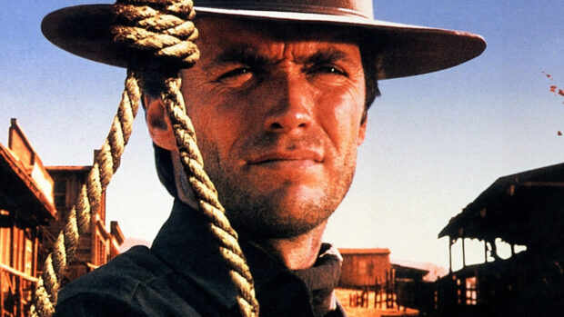 Clint Eastwood wearing a hat and looking serious in a western town with a rope hanging beside him