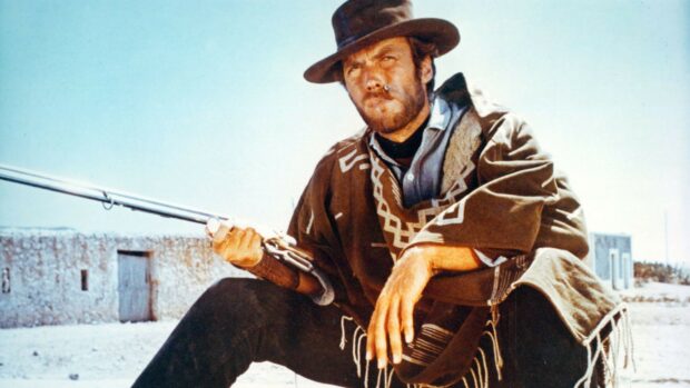 Clint Eastwood wearing a poncho and hat holding a rifle in a desert setting