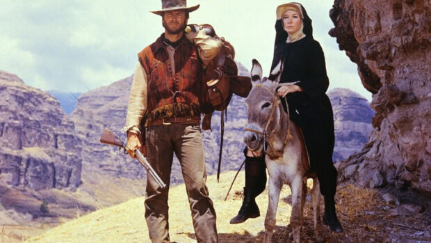 Clint Eastwood standing with a woman riding a donkey in a mountainous desert scene