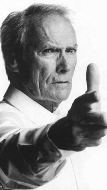 Clint Eastwood is making a finger gun gesture with a serious expression on his face