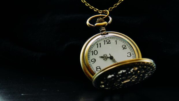 Antique clock with vintage design hanging on a chain over a dark background