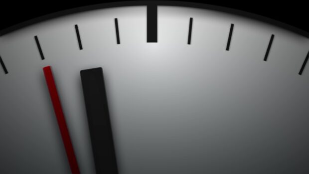 Close up of a clock with black and red hands showing the time near twelve