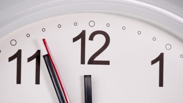 Close up of an analog clock showing time near twelve on a white dial with black numbers