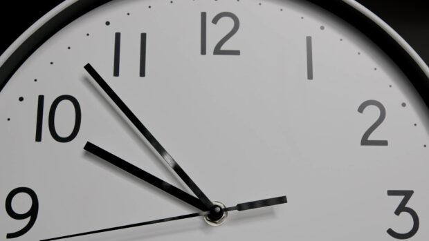 Close up of clock face with black hour minute and second hands showing time near eleven o clock