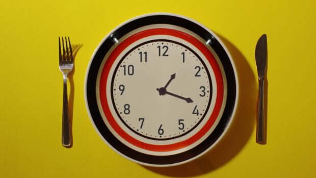 A clock design on a plate with fork and knife on a yellow surface showing time at four o'clock