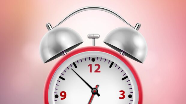 Red alarm clock with silver bells showing time near eleven o'clock on a pink background