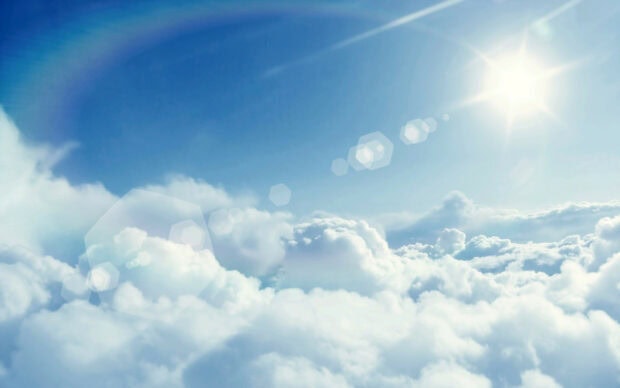 Fluffy clouds floating under bright sunlight in a clear blue sky with lens flare effects