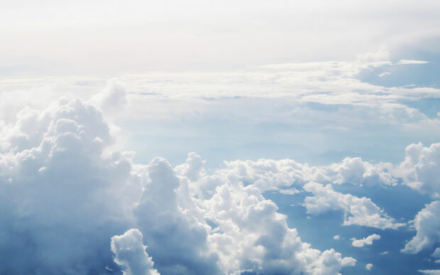 Fluffy white clouds form a peaceful sky scene above the horizon with soft light