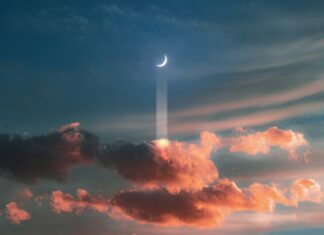 A crescent moon shines above colorful clouds during sunset with beams of light through the sky