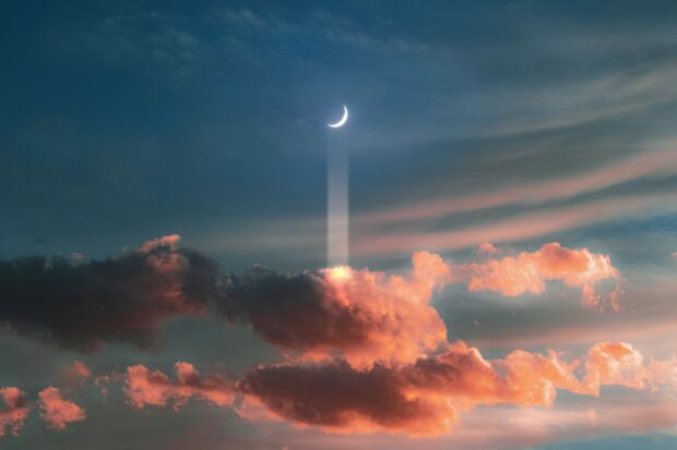 A crescent moon shines above colorful clouds during sunset with beams of light through the sky