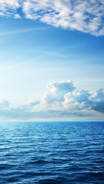 Fluffy clouds forming shapes over a calm ocean under a clear blue sky
