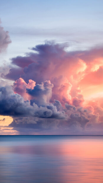 Pink and purple clouds over calm sea at sunset with soft reflections