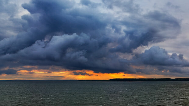 Dark clouds forming over the ocean during a dramatic sunset with orange sky hues