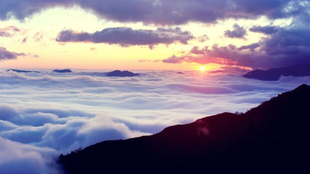 A sea of clouds covering mountains during a colorful sunset with clear clouds