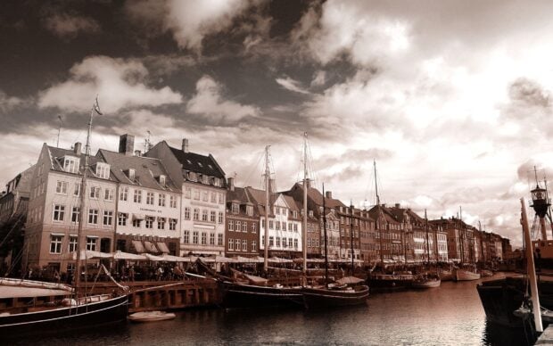 Historic waterfront buildings and boats in Copenhagen harbor under cloudy sky
