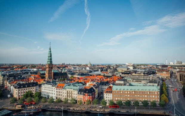 View of Copenhagen cityscape with historic buildings and church tower under a clear blue sky