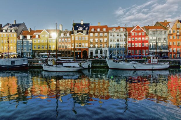 Colorful Copenhagen houses reflecting on the canal water with boats docked along the quay