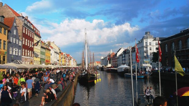 Colorful Copenhagen street with boats and crowd along the canal on a sunny day